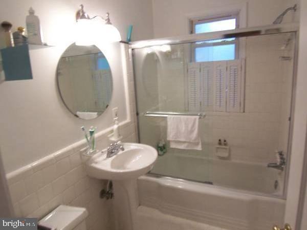 full bathroom featuring combined bath / shower with glass door, sink, tile walls, and toilet