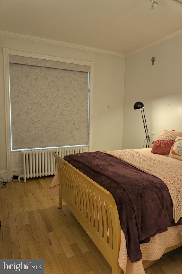 bedroom with ornamental molding, radiator heating unit, and light hardwood / wood-style floors