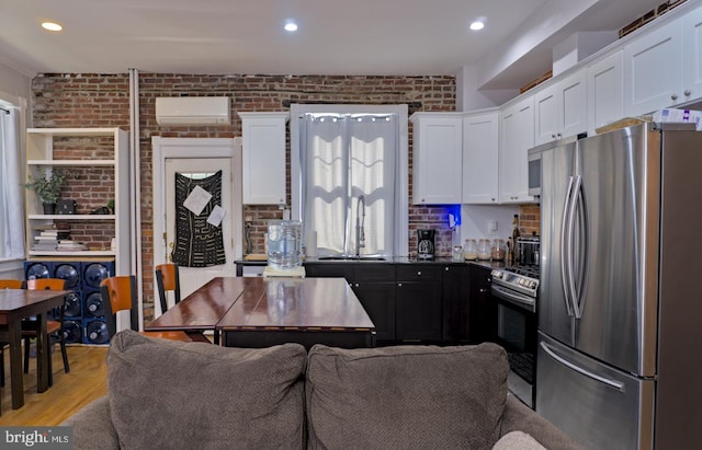 kitchen with appliances with stainless steel finishes, light wood-type flooring, white cabinetry, and an AC wall unit