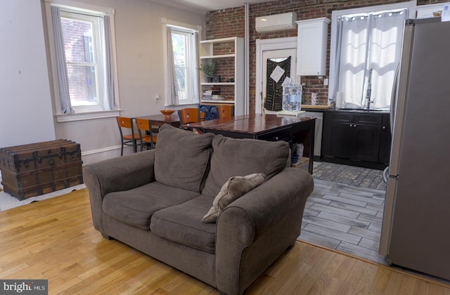 living room with brick wall, light hardwood / wood-style flooring, and a wall mounted AC