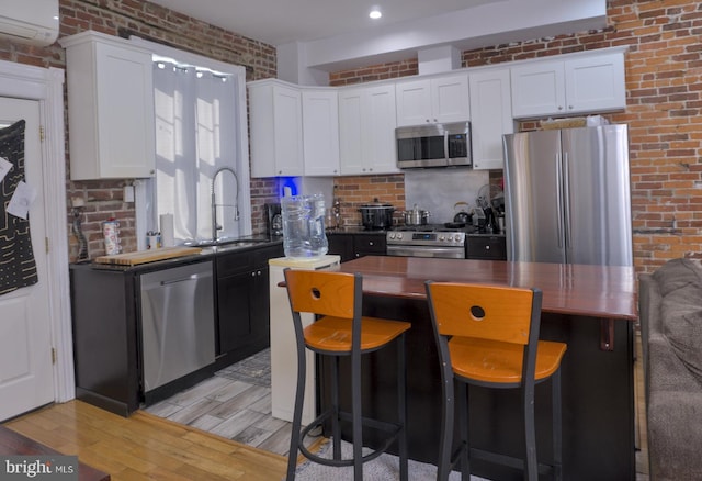 kitchen with stainless steel appliances, brick wall, light wood-type flooring, and white cabinetry