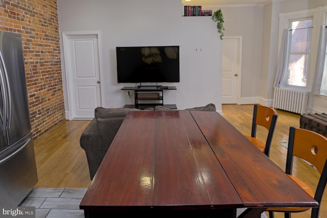 dining room featuring brick wall, radiator, light wood-type flooring, and crown molding