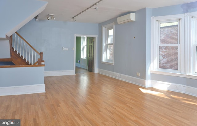 entryway with rail lighting, a wall mounted air conditioner, light wood-type flooring, and a healthy amount of sunlight