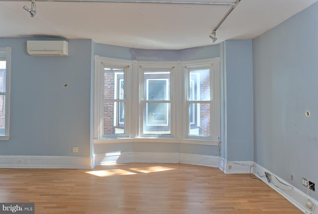 empty room featuring light wood-type flooring, a wall unit AC, and rail lighting