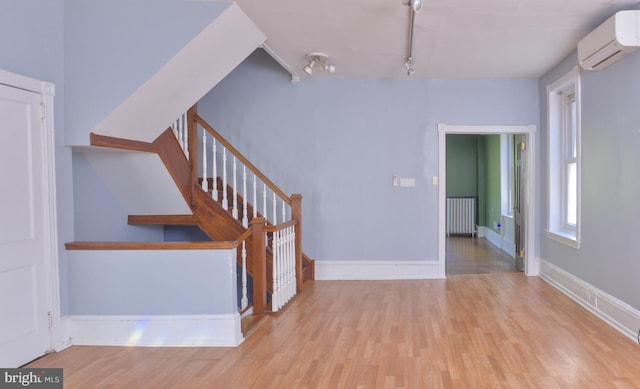 staircase featuring rail lighting, hardwood / wood-style flooring, radiator heating unit, and a wall mounted AC