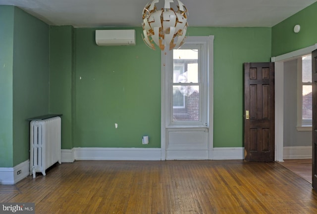 spare room featuring hardwood / wood-style flooring, a healthy amount of sunlight, radiator heating unit, and a wall mounted AC