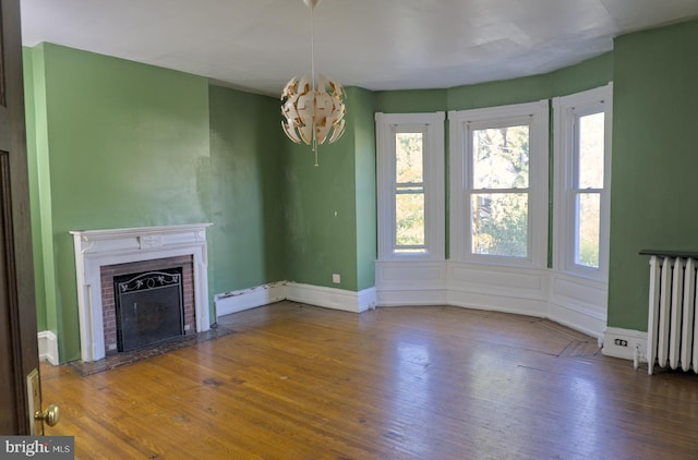 unfurnished living room with a brick fireplace, radiator heating unit, hardwood / wood-style floors, and a chandelier