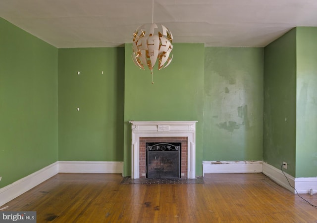 unfurnished living room with an inviting chandelier, wood-type flooring, and a brick fireplace