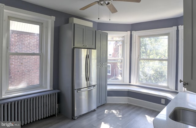 kitchen with stainless steel refrigerator, gray cabinetry, ceiling fan, radiator, and light hardwood / wood-style flooring