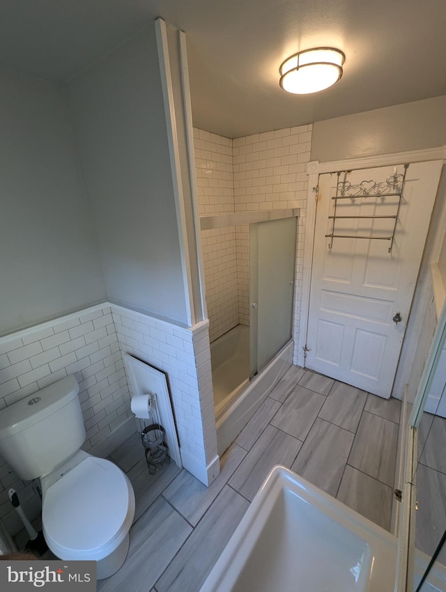 bathroom with a shower with door, toilet, and tile walls