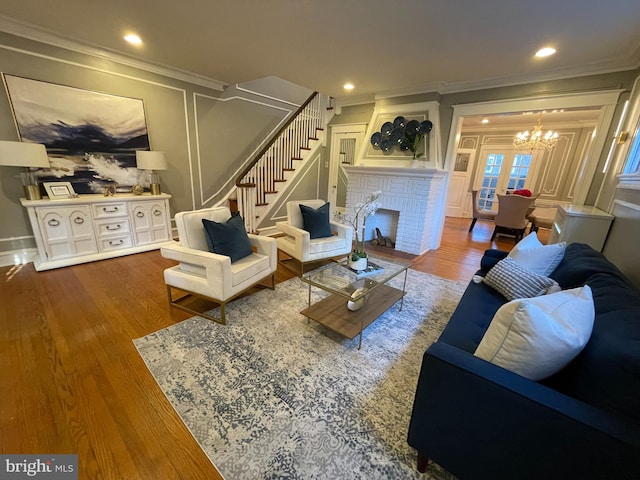 living room featuring a notable chandelier, ornamental molding, a brick fireplace, and hardwood / wood-style floors