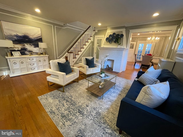 living room featuring crown molding, hardwood / wood-style flooring, an inviting chandelier, and a fireplace