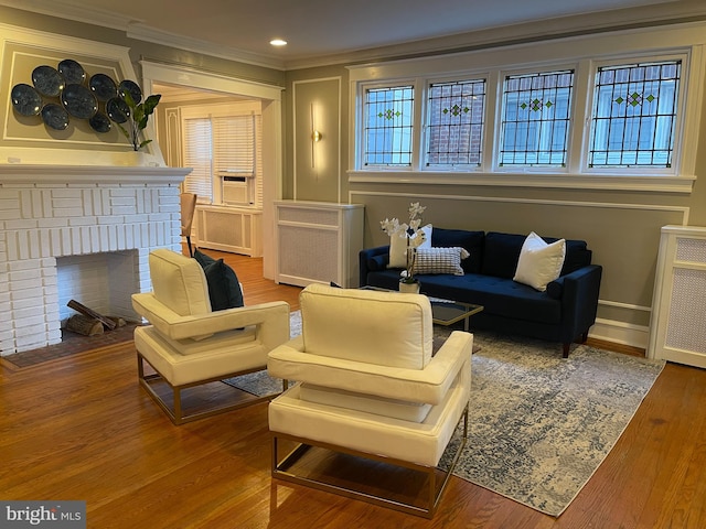 living area featuring ornamental molding, hardwood / wood-style floors, radiator heating unit, and a brick fireplace