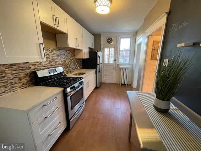 kitchen with stainless steel appliances, sink, hardwood / wood-style floors, white cabinets, and radiator heating unit