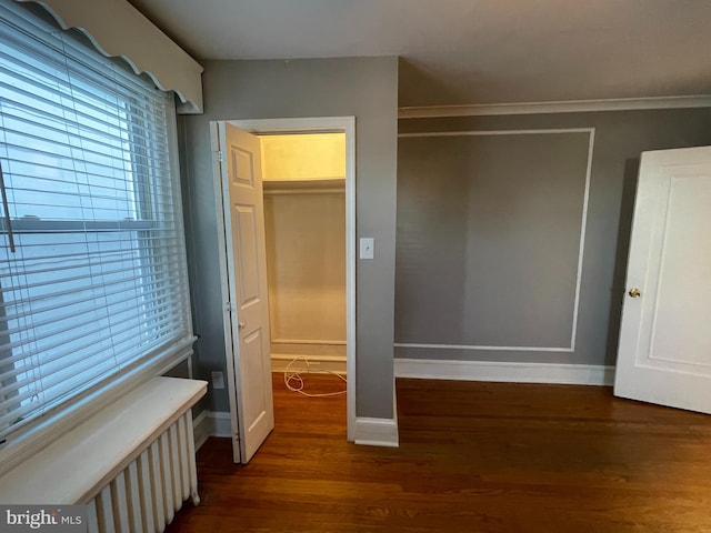 unfurnished bedroom with a closet, ornamental molding, a walk in closet, and dark hardwood / wood-style floors