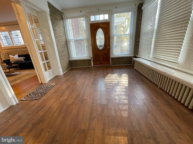 foyer entrance with brick wall, ornamental molding, and dark hardwood / wood-style flooring