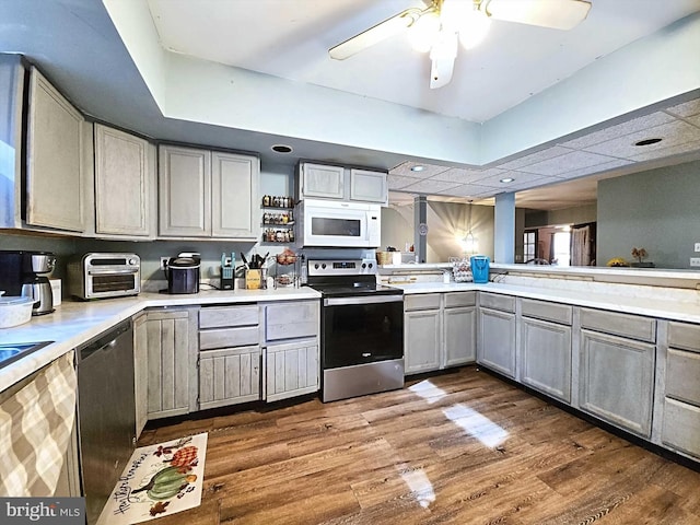 kitchen with stainless steel appliances, gray cabinets, hardwood / wood-style floors, kitchen peninsula, and ceiling fan