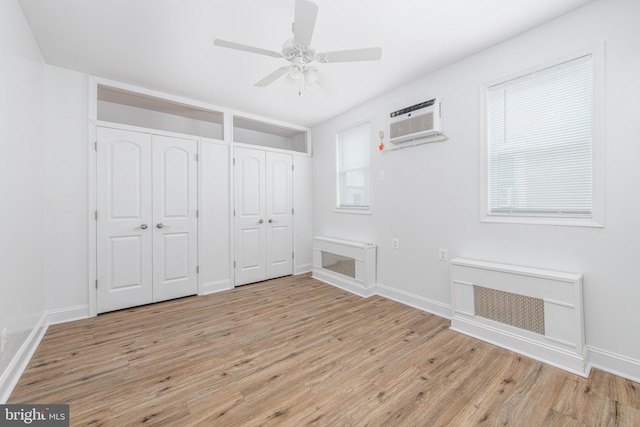 unfurnished bedroom featuring multiple closets, a wall mounted AC, light hardwood / wood-style flooring, and ceiling fan