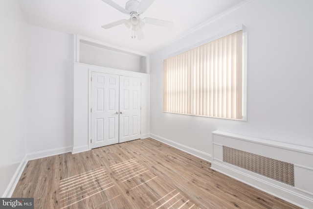 unfurnished bedroom with ceiling fan, radiator, a closet, and light wood-type flooring