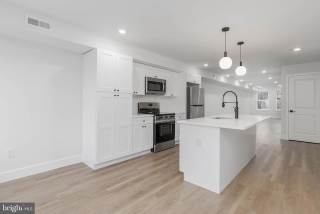 kitchen featuring sink, white cabinets, hanging light fixtures, stainless steel appliances, and a center island with sink