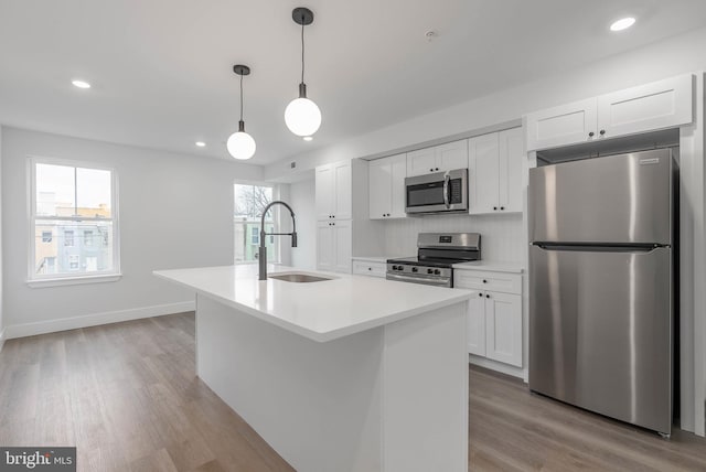 kitchen with an island with sink, appliances with stainless steel finishes, sink, and white cabinets