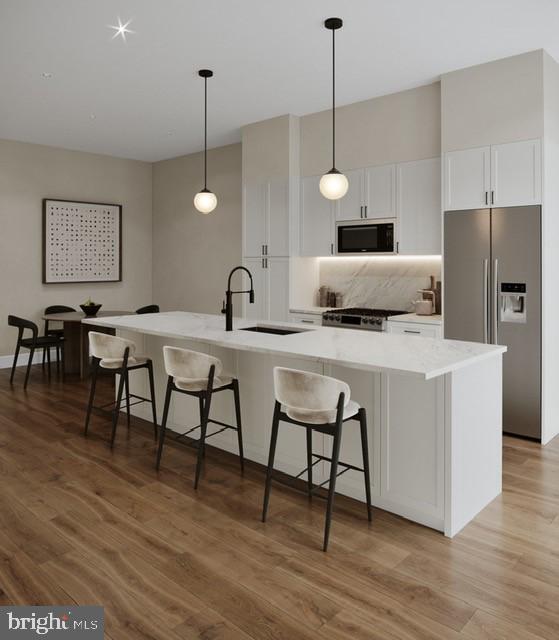 kitchen featuring black microwave, stainless steel refrigerator with ice dispenser, a large island with sink, and decorative light fixtures