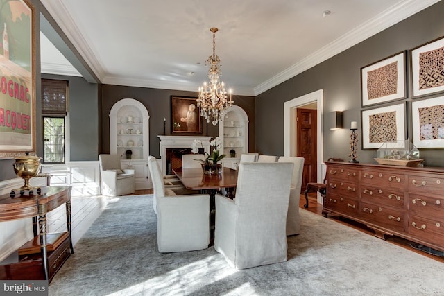 dining room featuring built in shelves, an inviting chandelier, crown molding, and hardwood / wood-style floors