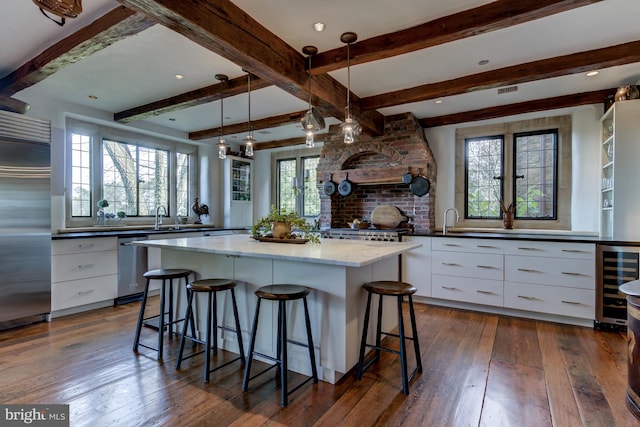 kitchen featuring wine cooler, hanging light fixtures, white cabinetry, appliances with stainless steel finishes, and a center island