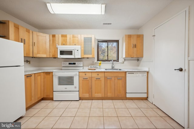 kitchen featuring white appliances, sink, light tile patterned floors, a textured ceiling, and light brown cabinetry