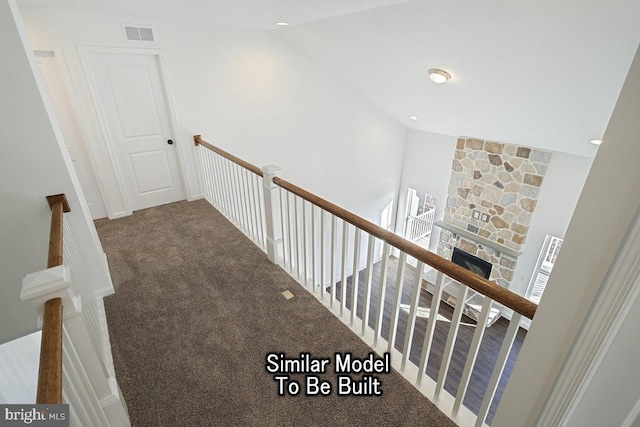 staircase with carpet floors, vaulted ceiling, and a stone fireplace