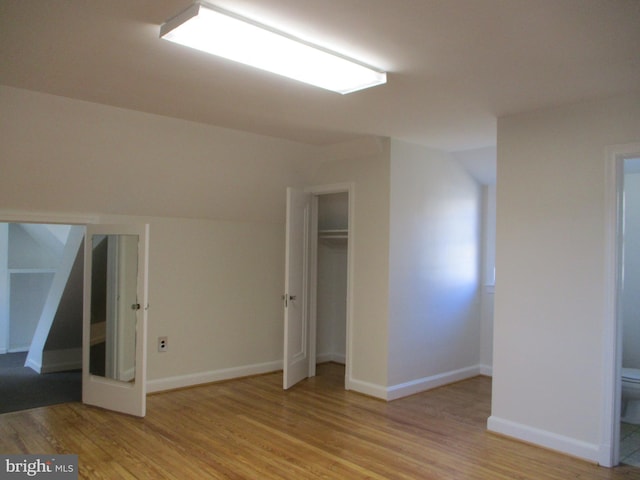 unfurnished bedroom with connected bathroom, light hardwood / wood-style flooring, and lofted ceiling