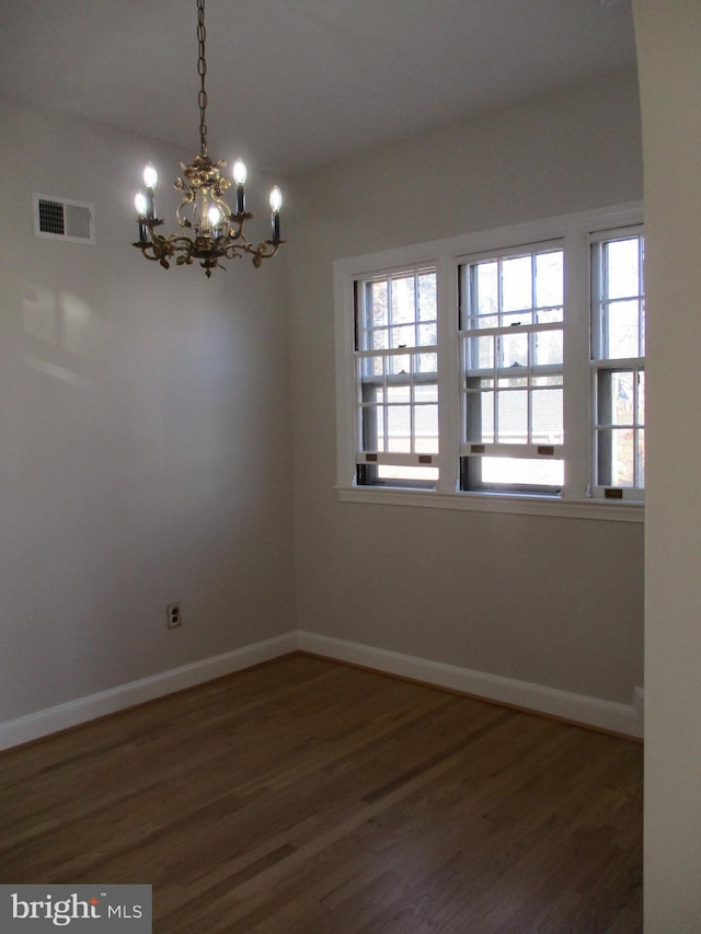 spare room with dark wood-type flooring, plenty of natural light, and a chandelier