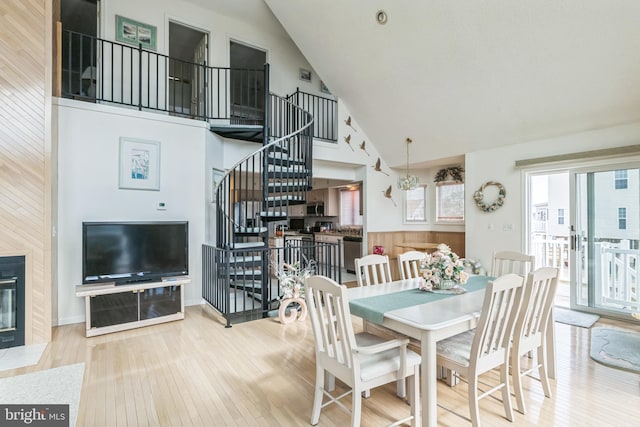 dining area featuring a fireplace, wood walls, light hardwood / wood-style floors, and high vaulted ceiling