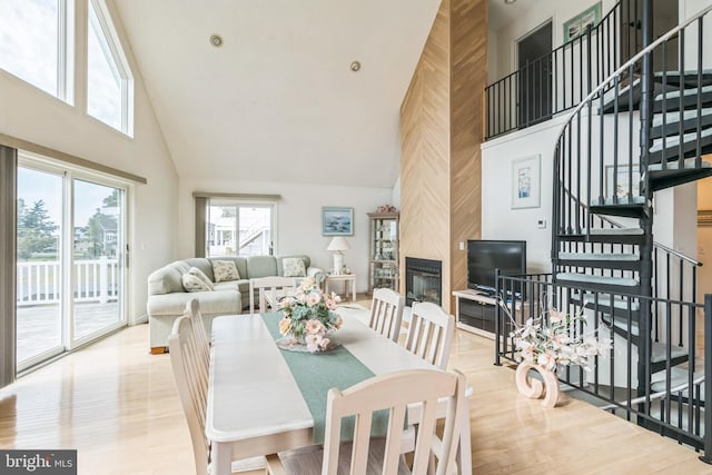 dining space with a fireplace, high vaulted ceiling, and light hardwood / wood-style flooring