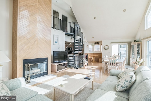 living room featuring high vaulted ceiling, wooden walls, a fireplace, and light hardwood / wood-style floors