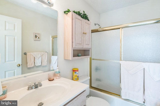 full bathroom featuring vanity, combined bath / shower with glass door, toilet, and a textured ceiling