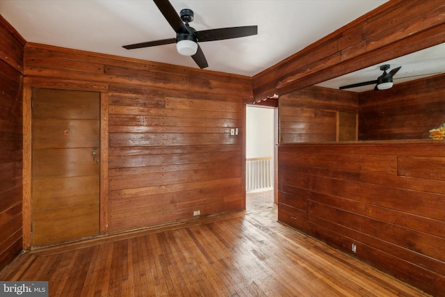 unfurnished room featuring ceiling fan, hardwood / wood-style flooring, and wood walls