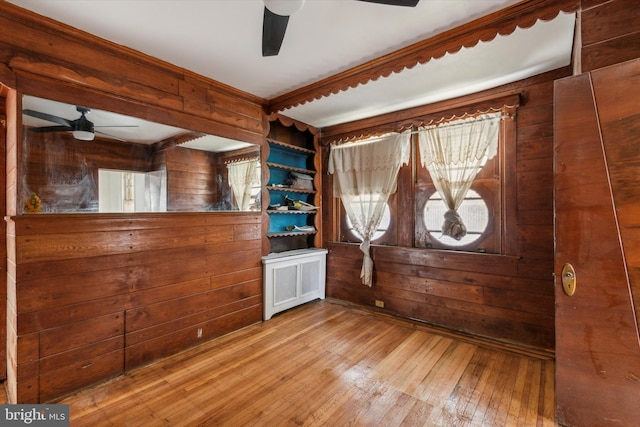 unfurnished room with wood walls, radiator, light wood-type flooring, and ceiling fan