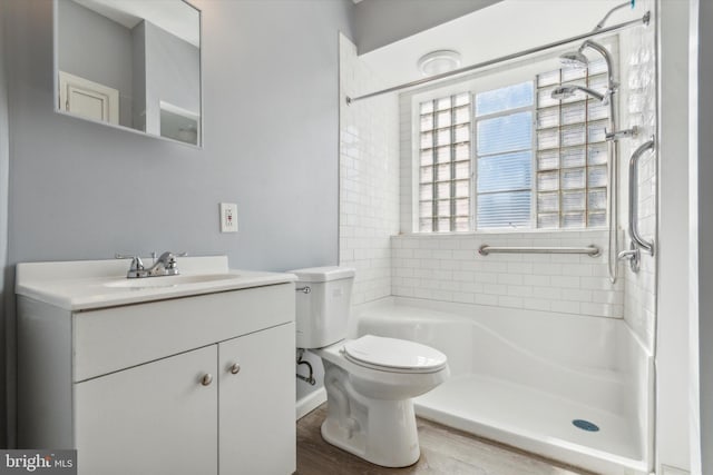 bathroom featuring hardwood / wood-style floors, a tile shower, toilet, and vanity