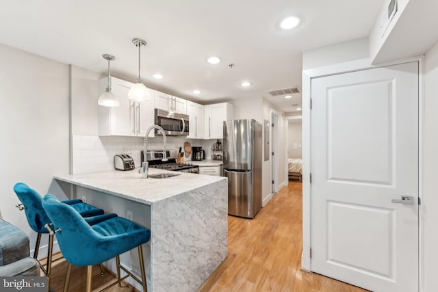 kitchen with appliances with stainless steel finishes, kitchen peninsula, light hardwood / wood-style floors, pendant lighting, and white cabinets