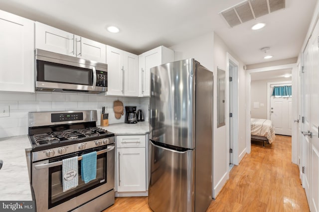 kitchen with white cabinetry, backsplash, stainless steel appliances, and light wood-type flooring