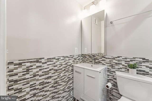 bathroom featuring toilet, vanity, and tile walls