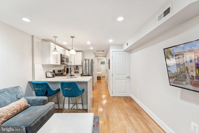 kitchen featuring a breakfast bar area, hanging light fixtures, stainless steel appliances, kitchen peninsula, and white cabinetry