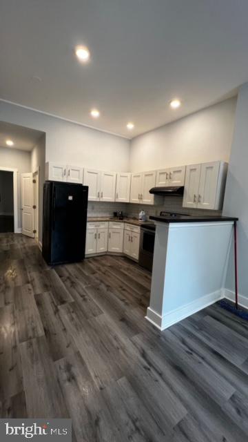 kitchen featuring dark countertops, dark wood finished floors, freestanding refrigerator, and under cabinet range hood