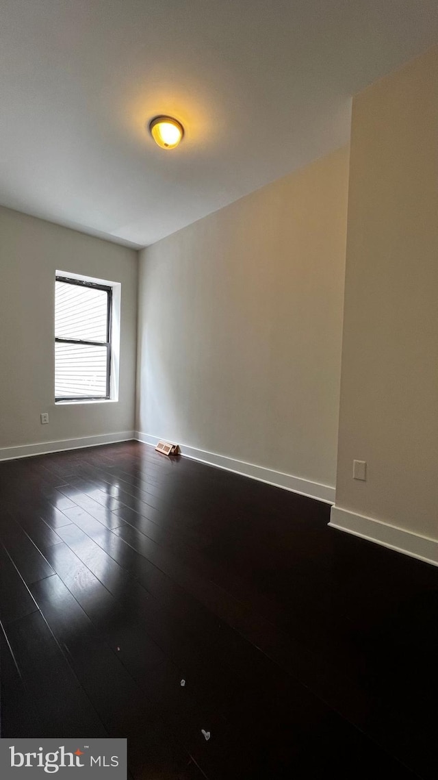 empty room featuring baseboards and dark wood finished floors