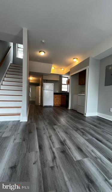 unfurnished living room with independent washer and dryer, baseboards, dark wood-style floors, and stairway