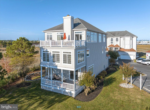 rear view of property featuring a balcony, a garage, and a lawn