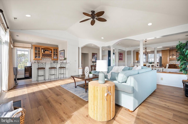 living room featuring vaulted ceiling, ornate columns, ceiling fan with notable chandelier, and light hardwood / wood-style floors