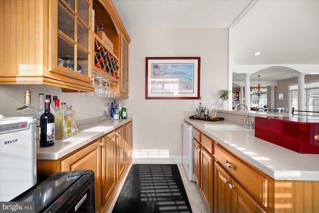 kitchen with light tile patterned floors, a chandelier, white dishwasher, decorative columns, and sink