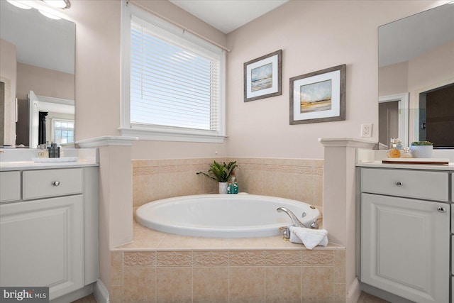 bathroom with vanity, tiled tub, and a healthy amount of sunlight